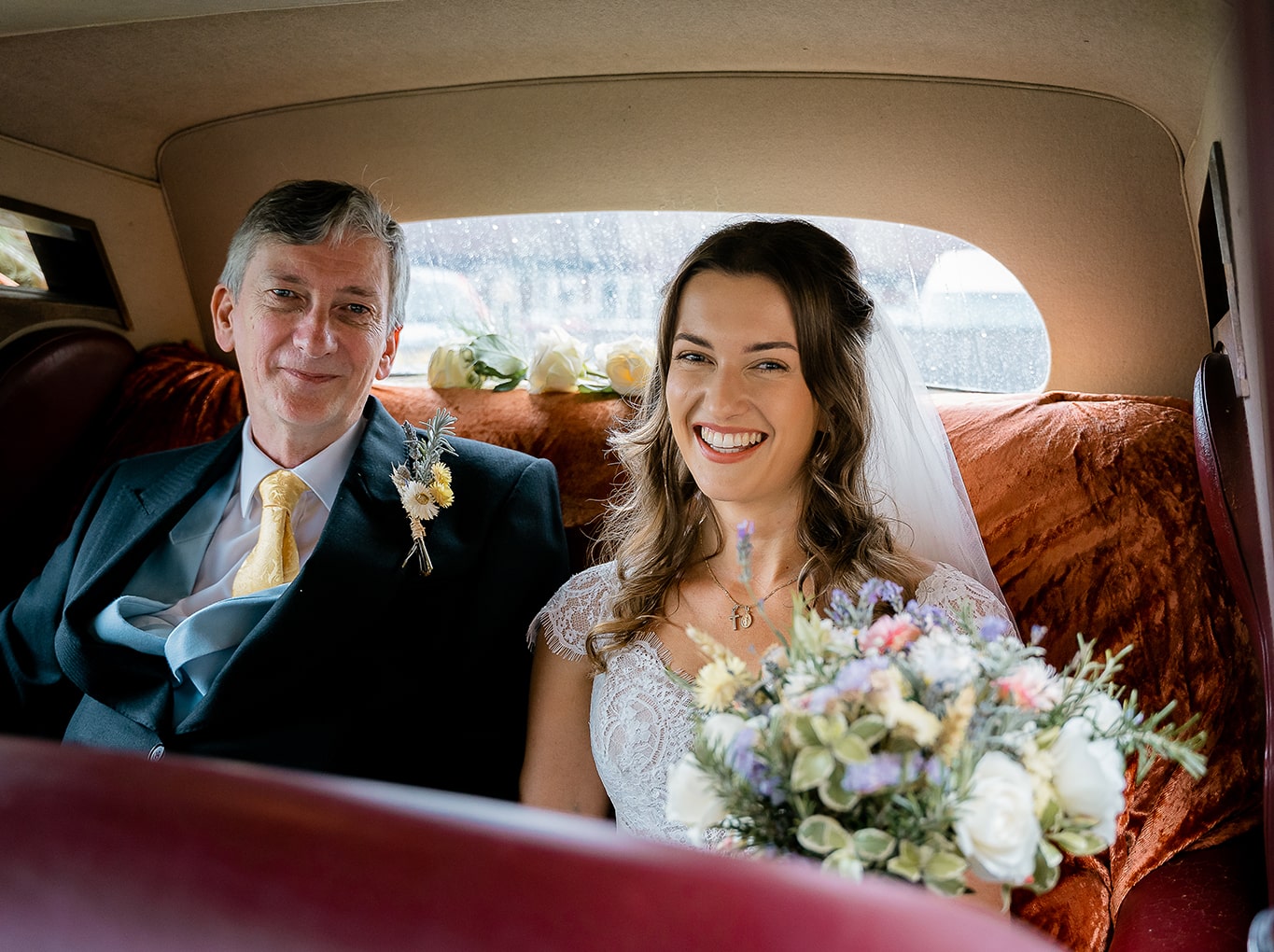 Smiling bride and her father enjoying their journey to the wedding in chauffer driven vintage car