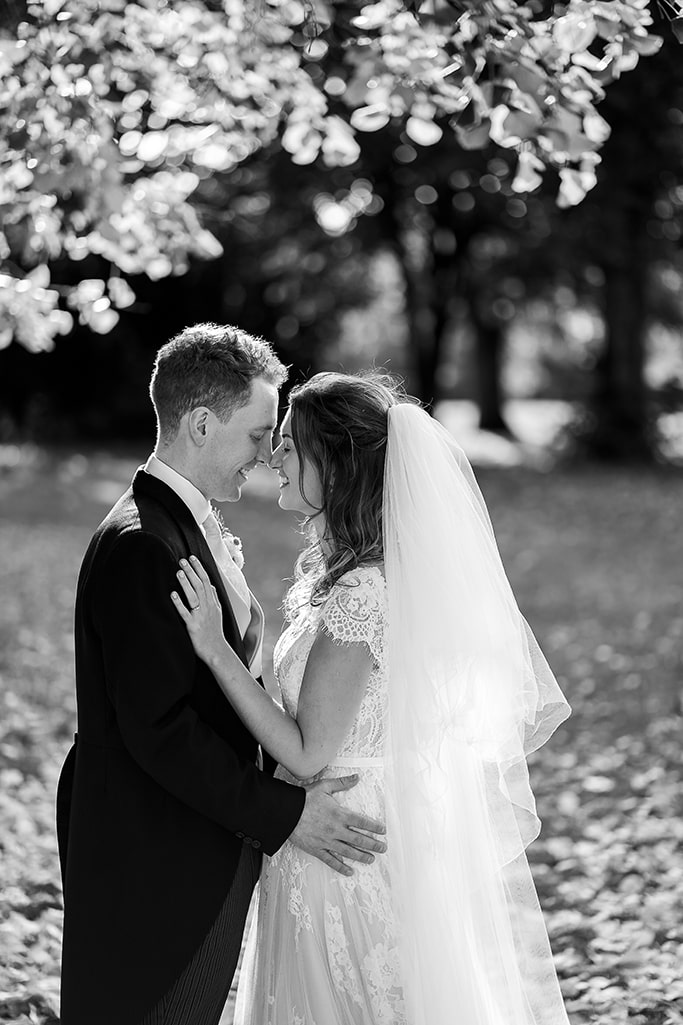2 of 3 - black and white photo groom and bride standing face-to-face in park with their noses touching