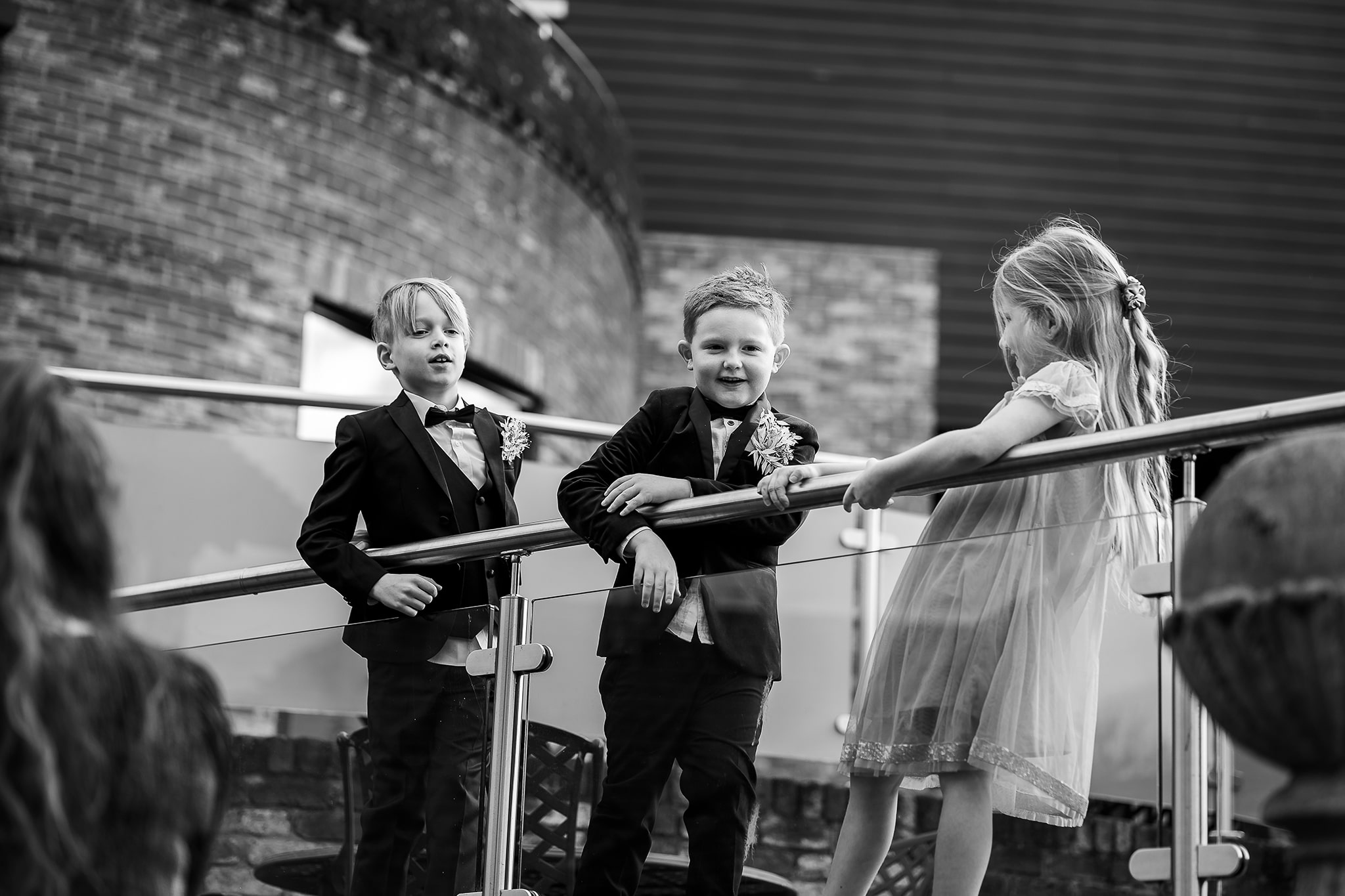 Contemporary black and white candid photo of children standing on balcony at Old Thorns enjoying the wedding
