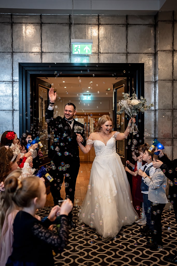 Fun candid image of bride and groom being sprayed with bubbles by all the guest children at their wedding