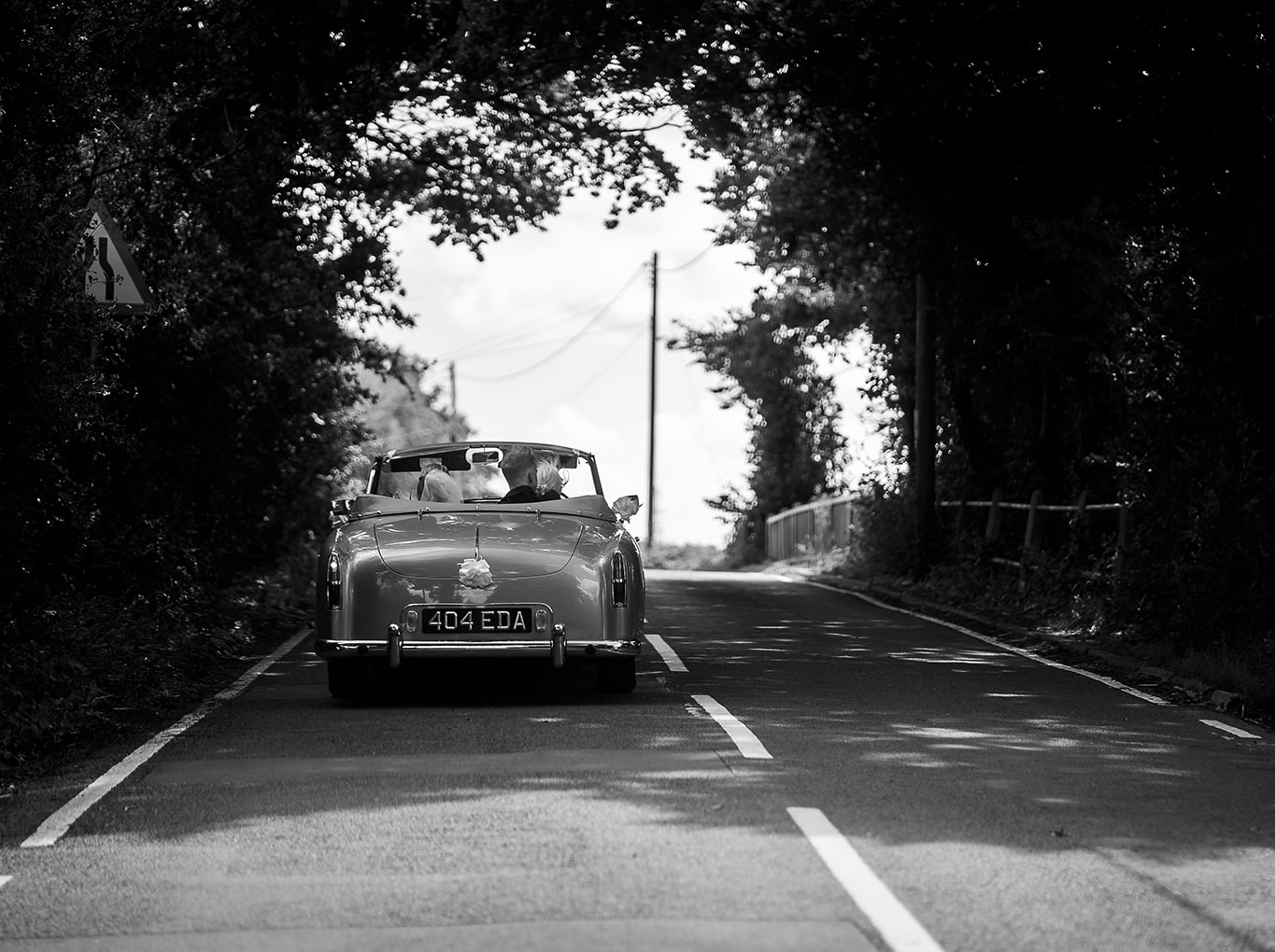 Black and white photo of married couple being driven in vintage car heading down Hampshire country road