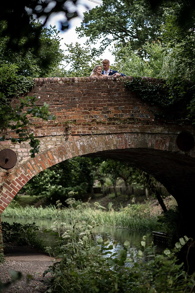 Married couple standing on a small old brick-arched bridge over a small narrow river