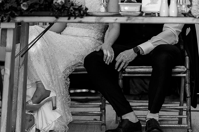 Romantic black and white under-table shot of bride with her hand on grooms leg