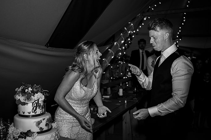 Black and white photo of bride and groom laughing during the cutting of the cake ceremony