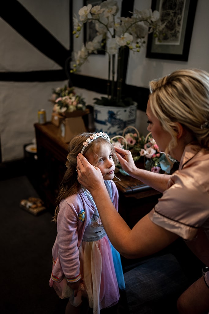 Cute little bridesmaid being assisted with her floral headband by her bride (mother)