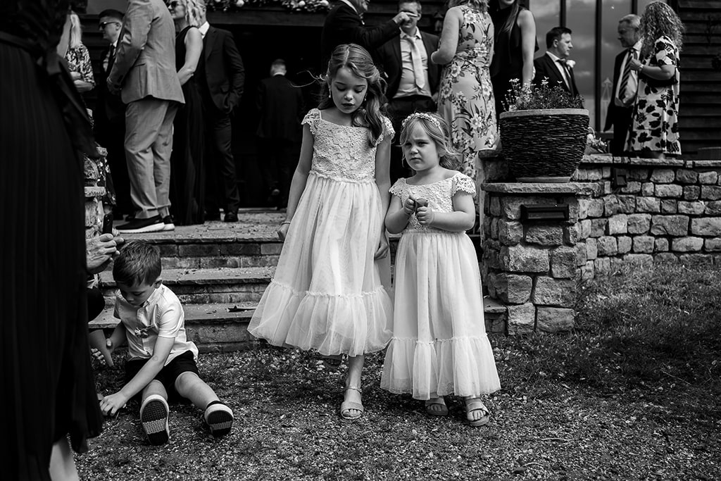 Black and white photo of two sweet little girl bridesmaids walking down some garden steps with other guests in the background