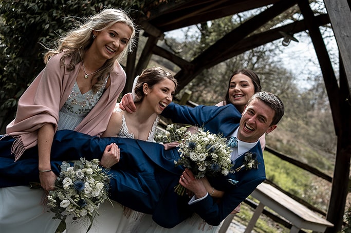 Funny photo of laughing bride and her two amused bridesmaids lifting up the laughing groom