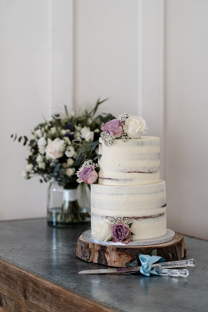 Contemporary white two-tier wedding cake decorated with several rose buds, laid on a sliced decorative rustic timber log
